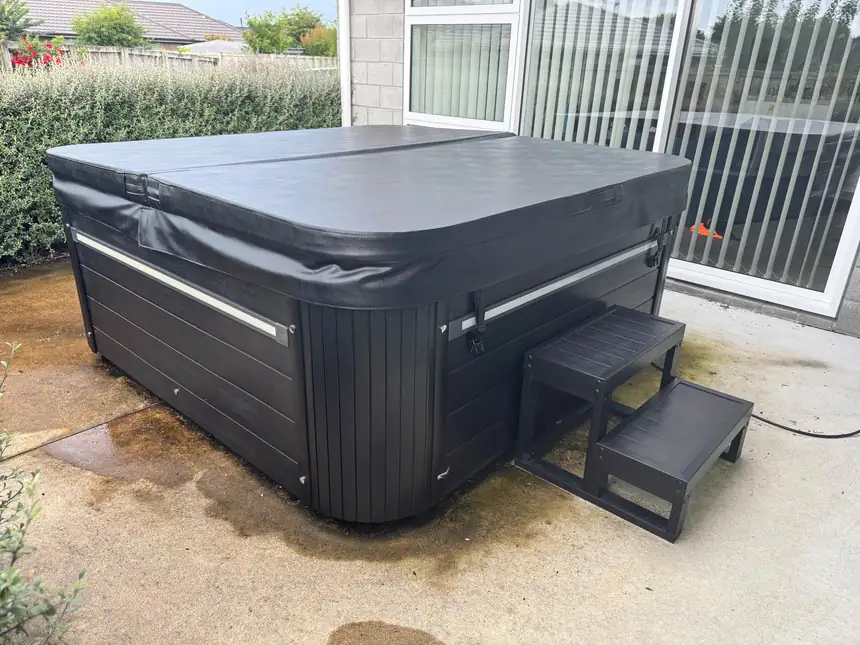A spa pool sited on a concrete pad beside a house, cover on and steps in place