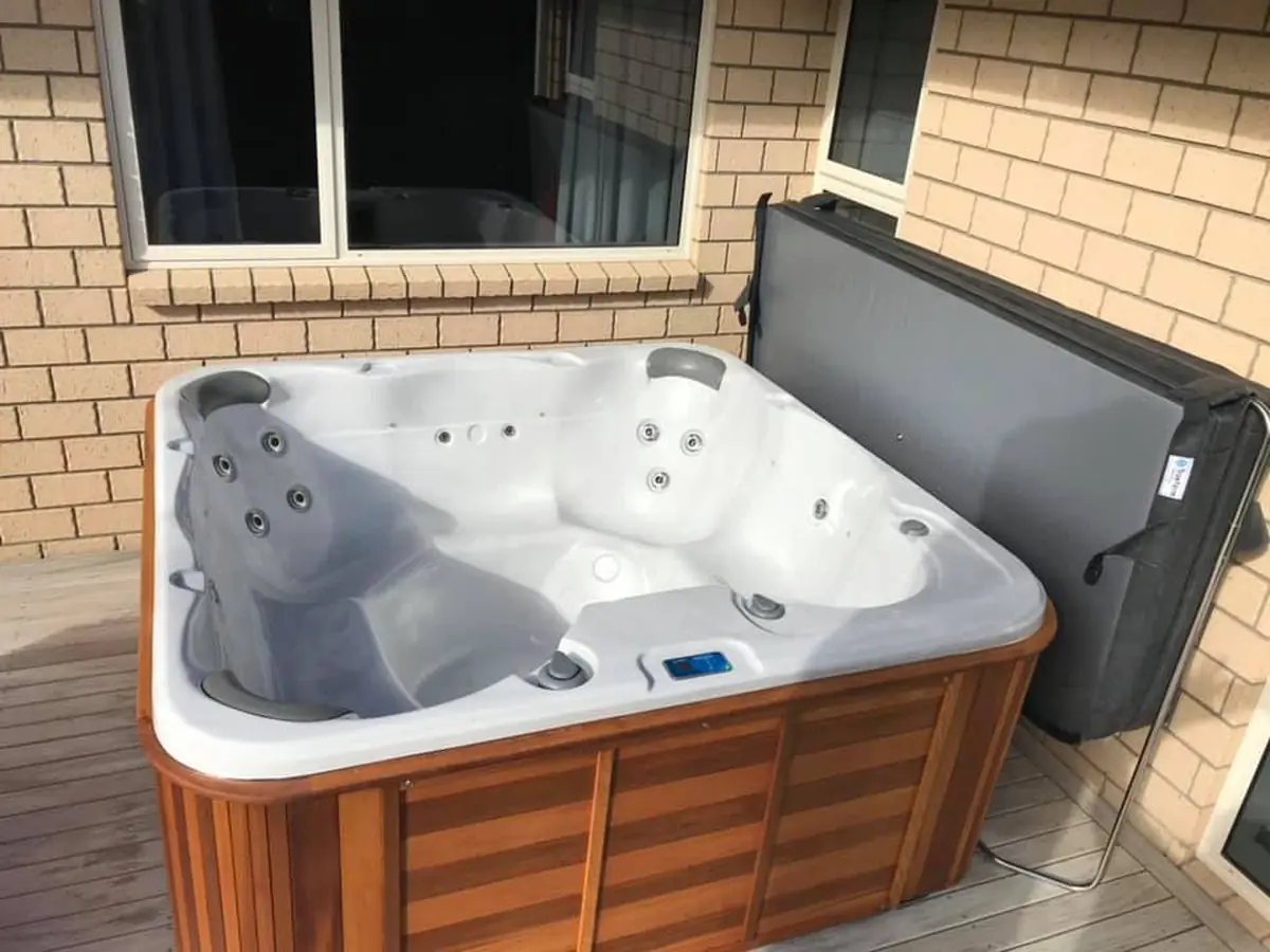 A spa pool on a deck against a brick wall, cover propped open